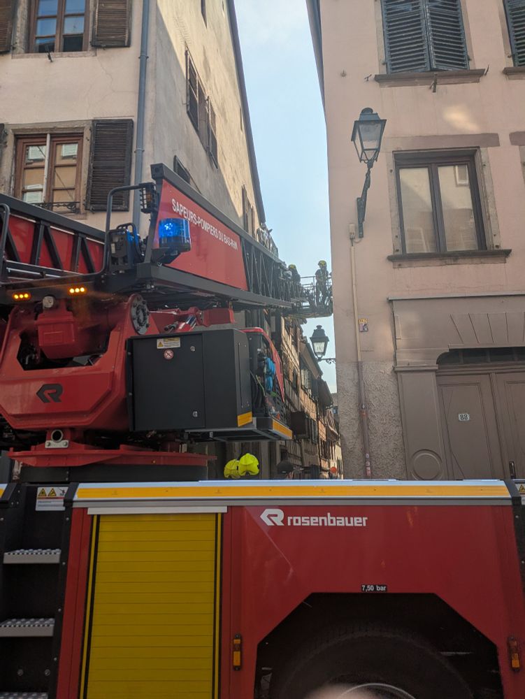 Échelle de pompier levée dans un ruelle très étroite. Deux pompiers en haut sur une plateforme.