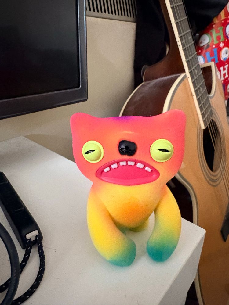 A multicoloured motion detecting Fart Fuggler. Its eyes are squinting and its top row of teeth are showing.