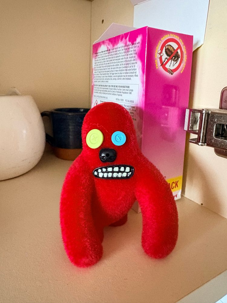 A red coloured motion detecting Fart Fuggler. Its eyes has yellow and blue buttons for eyes and it’s mouth shows a grimace.