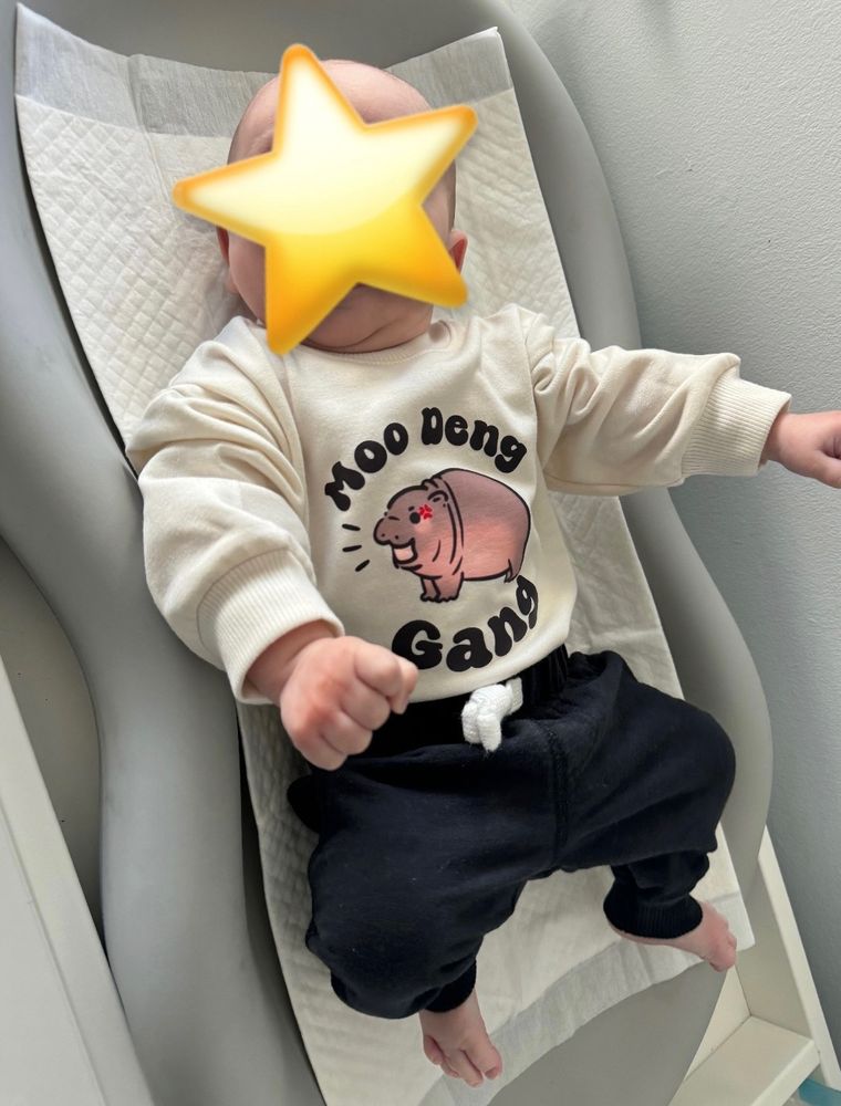 a baby in a shirt that says “moo deng gang” with a drawing of moo deng