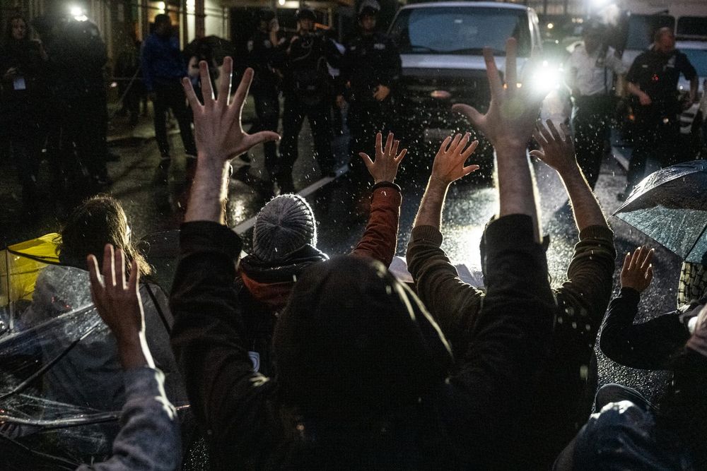 protesters sitting in the middle of the street blocking an ICE van with their hands up