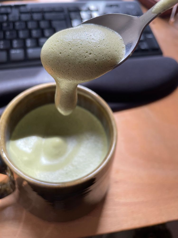 Foamy green gloop dripping off a spoon into a mug of more foamy green gloop. 