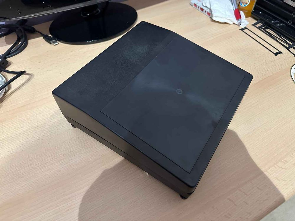 A black plastic project enclosure with a sloping top on a beach wood desk. The box has no other significant features as it has not yet been used. 