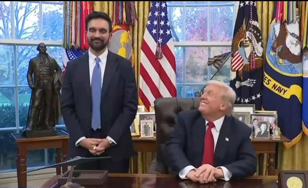 Trump sits at the Resolute Desk in the Oval Office while Mamdani stands next to him. Trump is absolutely BEAMING at Mamdani like a hardcore fan boy.