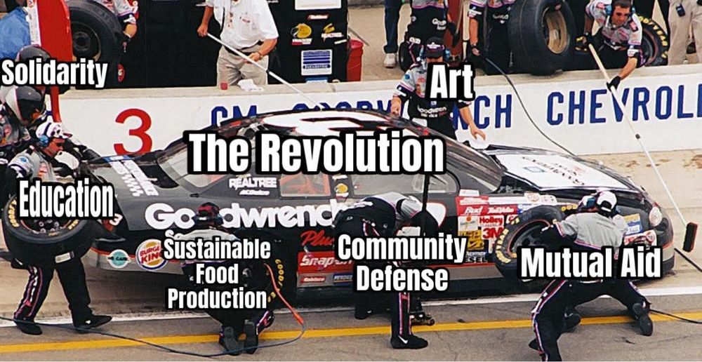 A screencap of a NASCAR race. The pit crew surrounds the pulled-over car, labeled "The Revolution". Each crew member reads: "Solidarity", "Education", "Sustainable Food Production", "Community Defense", "Mutual Aid", and "Art".