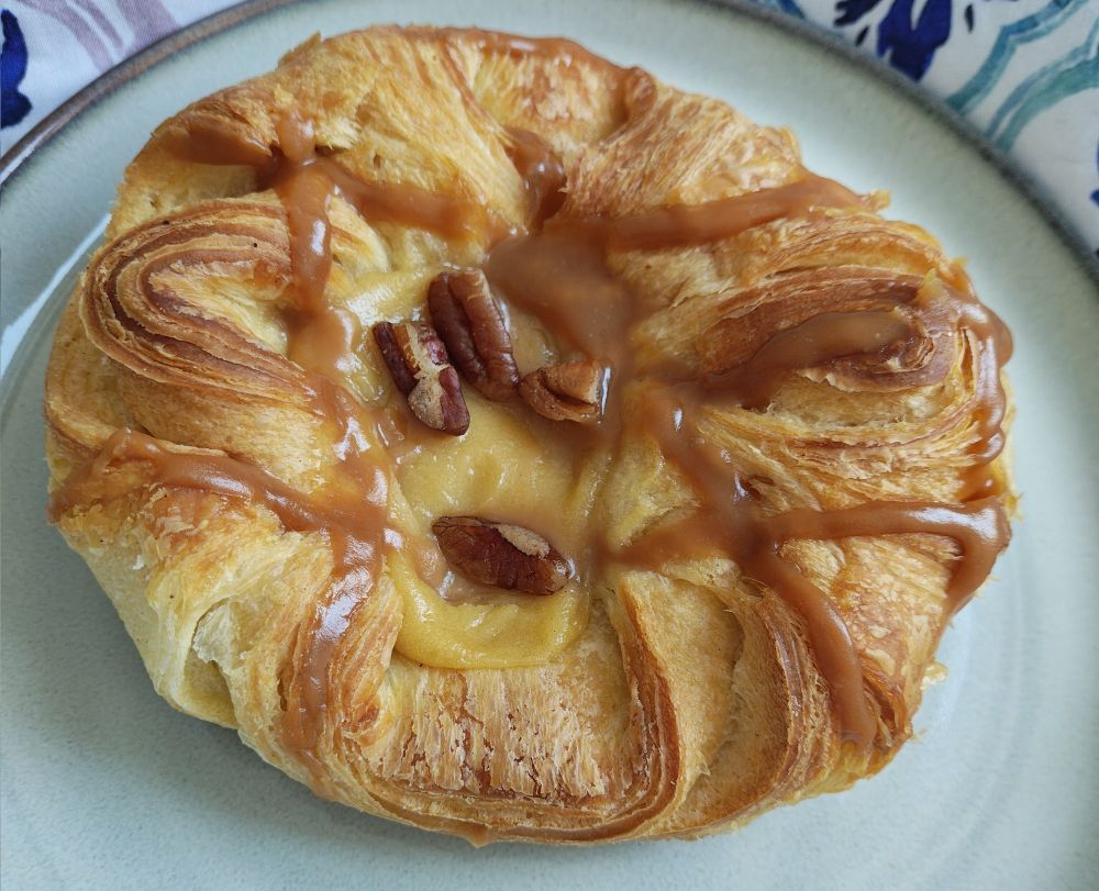 A large Danish pastry with drizzles of caramel all over and a pecan center.