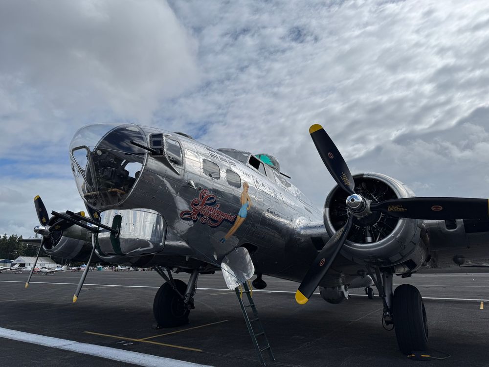The front of the Sentimental Journey, a B17 with Betty Grable painted on the nose. Three of its four 9-cylinder Wright engines can be seen with their three-blade propellers, and the forward gun turret with its two 50-caliber guns are in the foreground. It is parked with the access ladder extended. 