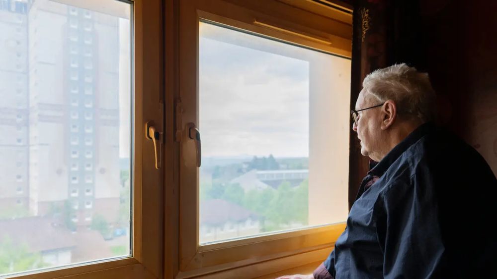 Picture of an older person looking out the window on a rainy day.