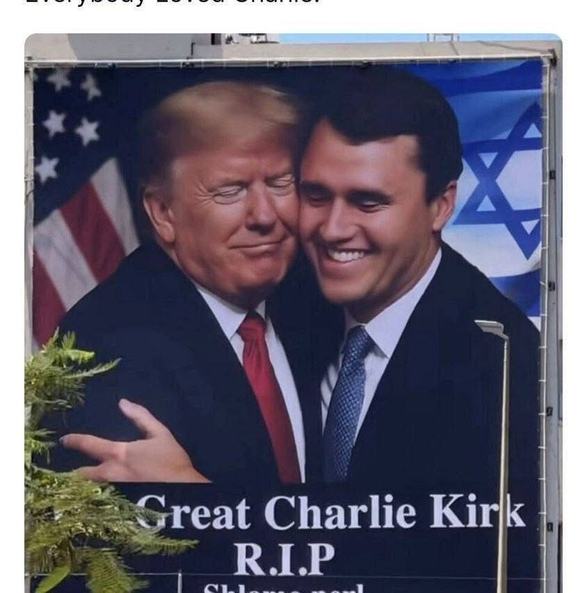A giant banner (a billboard ad?), showing Donald Trump and Charlie Kirk both smiling, embracing cheek to cheek with a U.S. flag behind Trump and the Israeli flag behind Kirk. There is a caption, partially obscured by a plant or tree, "The Great Charlie Kirk R.I.P."