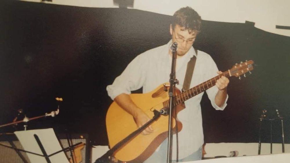 A twenty something me playing a Tacoma road king guitar on a stage.
