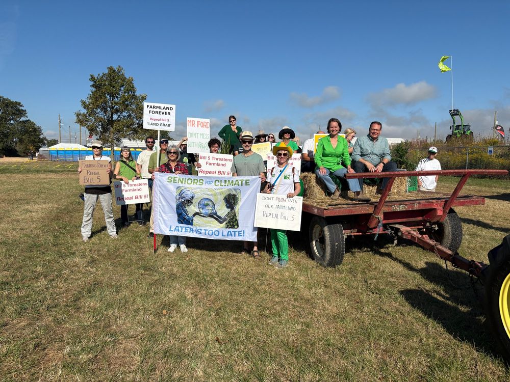 A photo of Mike and Aislinn with the group at the Green float. The group members are holding signs that read "Seniors for Climate" "Farmland Forever" and "Bill 5 Threatens Farmland"
