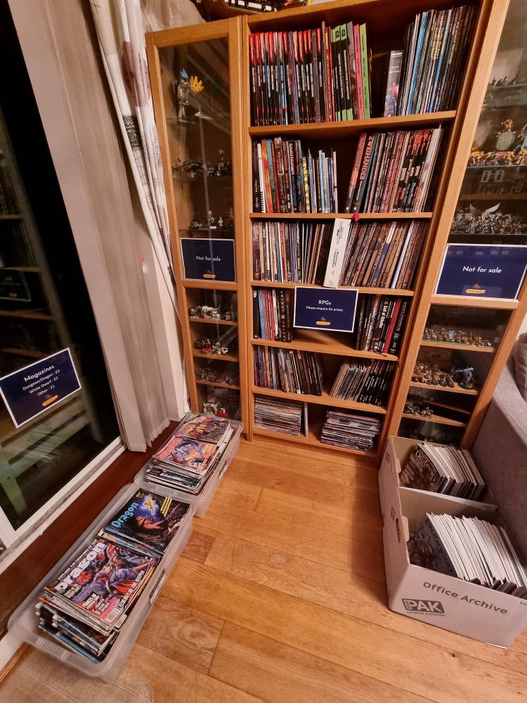 Bookcases covered in RPGs, with rummage boxes of old rpg magazines and white dwarf underneath 