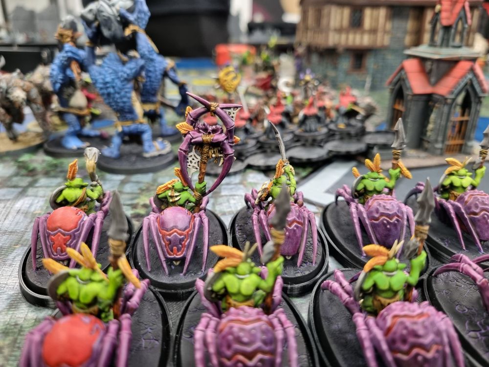 A gloomspite gitz army on the table, in the distance troggoths fight rat ogors.