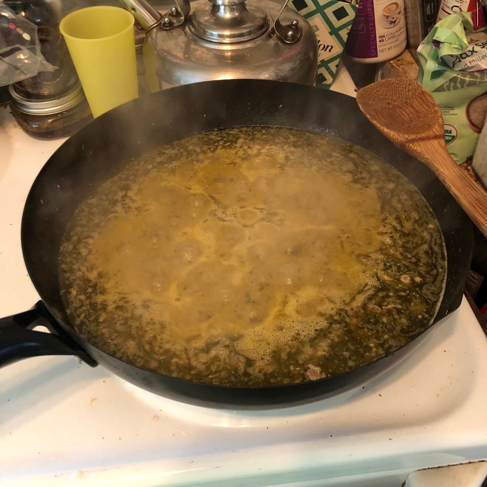 A wok full of boiling food atop a stove.