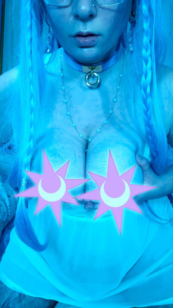 Picture of nonbinary FTM femboy fairy Stellaris with their long blue hair braided elf wig and a lavender collar with gold o-ring hardware. They are wearing pastel mint colored mesh and lace lingerie with the top pulled down below their tits, which they are cupping towards the camera. Purple and blue moon and star graphics hide their nipples from view. A pearl necklace dips temptingly between their soft breasts. They are wearing crystal moon and star earrings, and opal nose ring, and the bottom half of their large, geometric glasses frames can be seen before the upper half of their face is cut off from view. Their lips are slightly parted, plush, glossy, shiny, and oh so delicious looking.