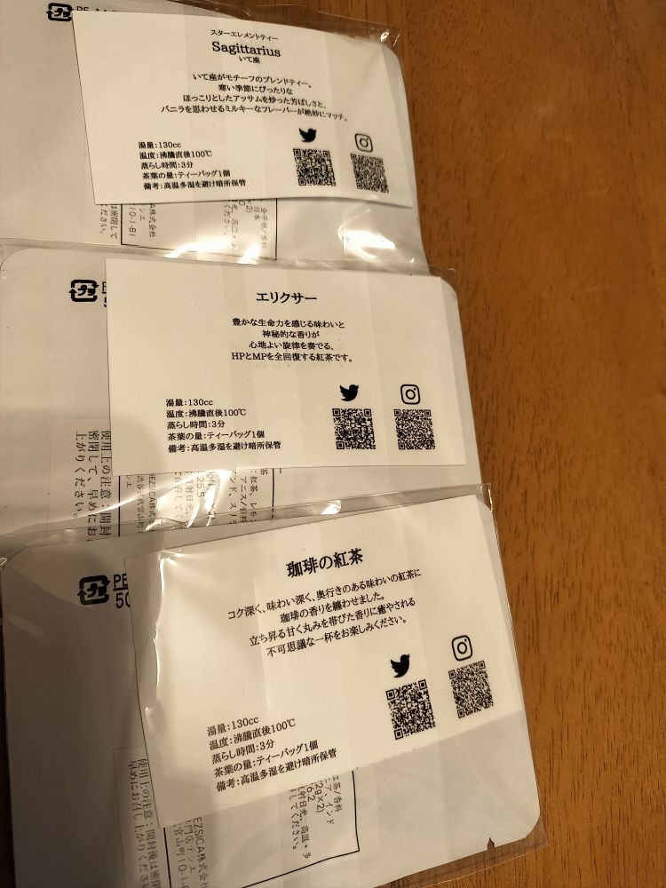 ティーパックが裏側にして3つ並べられている　中の紙には説明文が記載されている。説明文は上から「スターエレメントティー Sagittarius いて座 いて座がモチーフのブレンドティー。寒い季節にぴったりなほっこりとしたアッサムを炒った芳ばしさとバニラを思わせるミルキーなフレーバーが絶妙にマッチ。」、「エリクサー 豊かな生命力を感じる味わいと神秘的な香りが心地よい旋律を奏でる、HPとMPを全回復する紅茶です。」、「珈琲の紅茶 コク深く、味わい深く、奥行きのある味わいの紅茶に珈琲の香りを纏わせました。立ち昇る甘く丸みを帯びた香りに癒やされる不可思議な一杯をお楽しみください。」