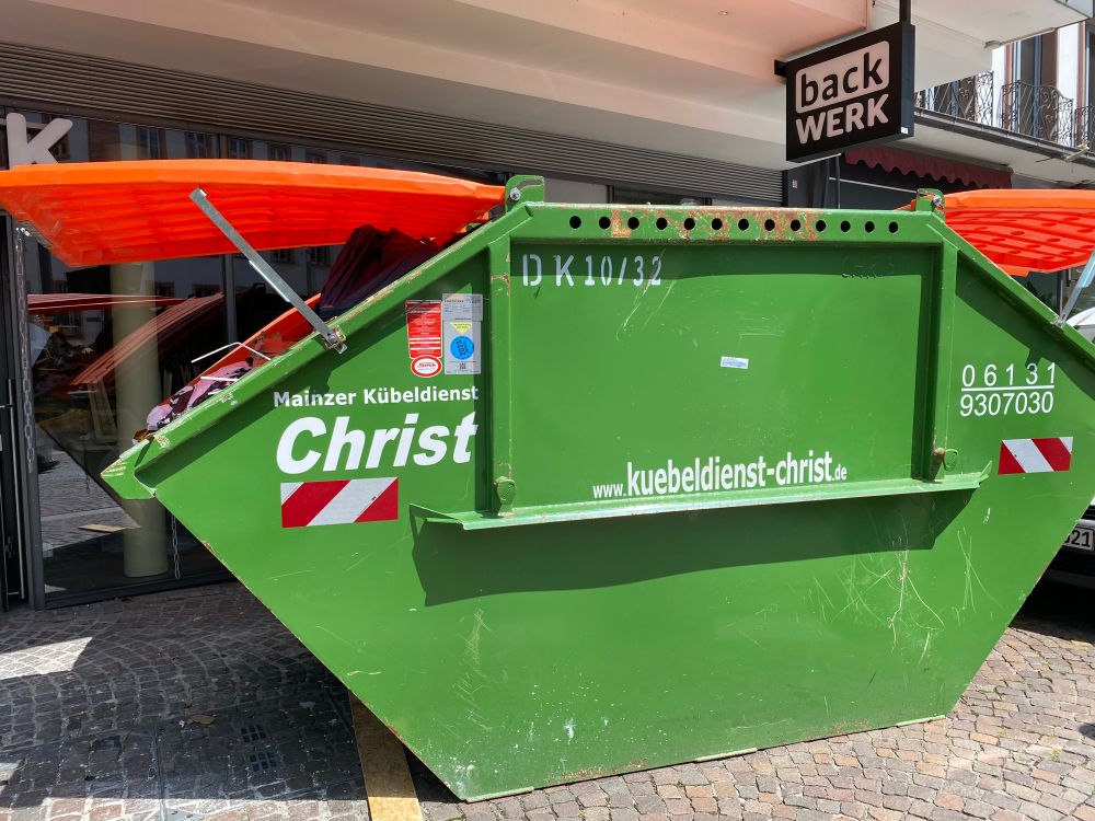 A green skip with Christ written on it outside a Back Werk - red plastic is sticking out of both sides