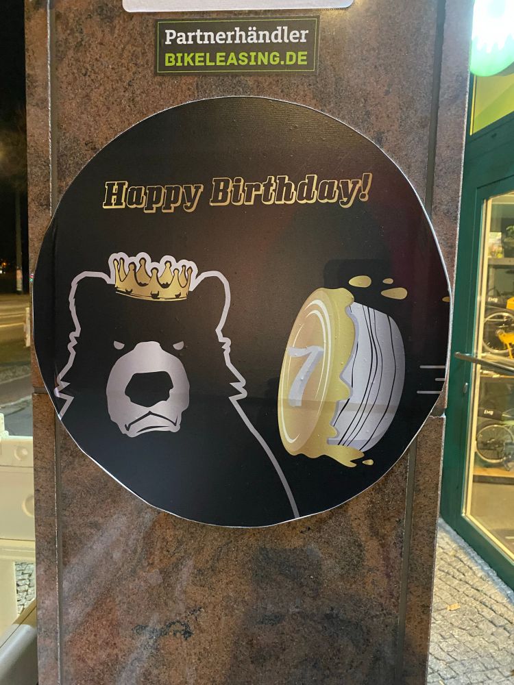 A grumpy bear wearing a crown about to be hit in the face with a pie with the number 7 on it with the words ‘Happy Birthday’ at the top