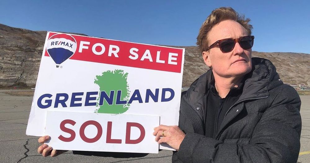 Conan O'Brien in Greenland holding a "for sale, Greenland" sign on an episode of Conan Without Borders from 2019