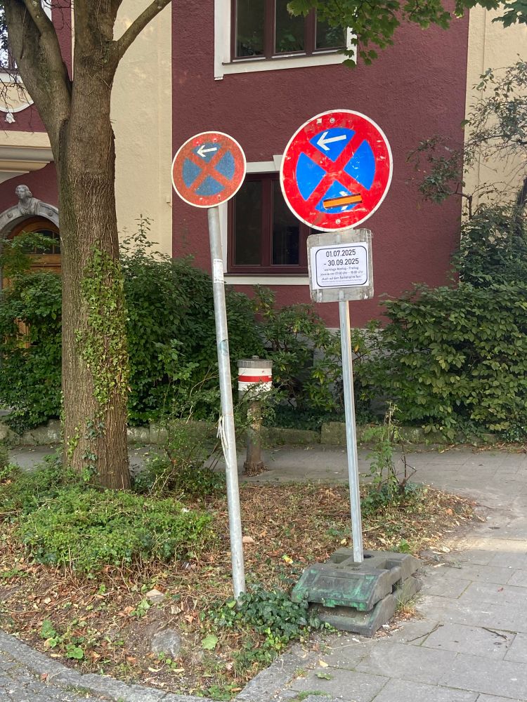 Neben einem fest montierten absolutes-Halteverbot-Schild steht ein temporäres (mobiles) absolutes-Halteverbot-Schild mit einem definierten Zeitraum