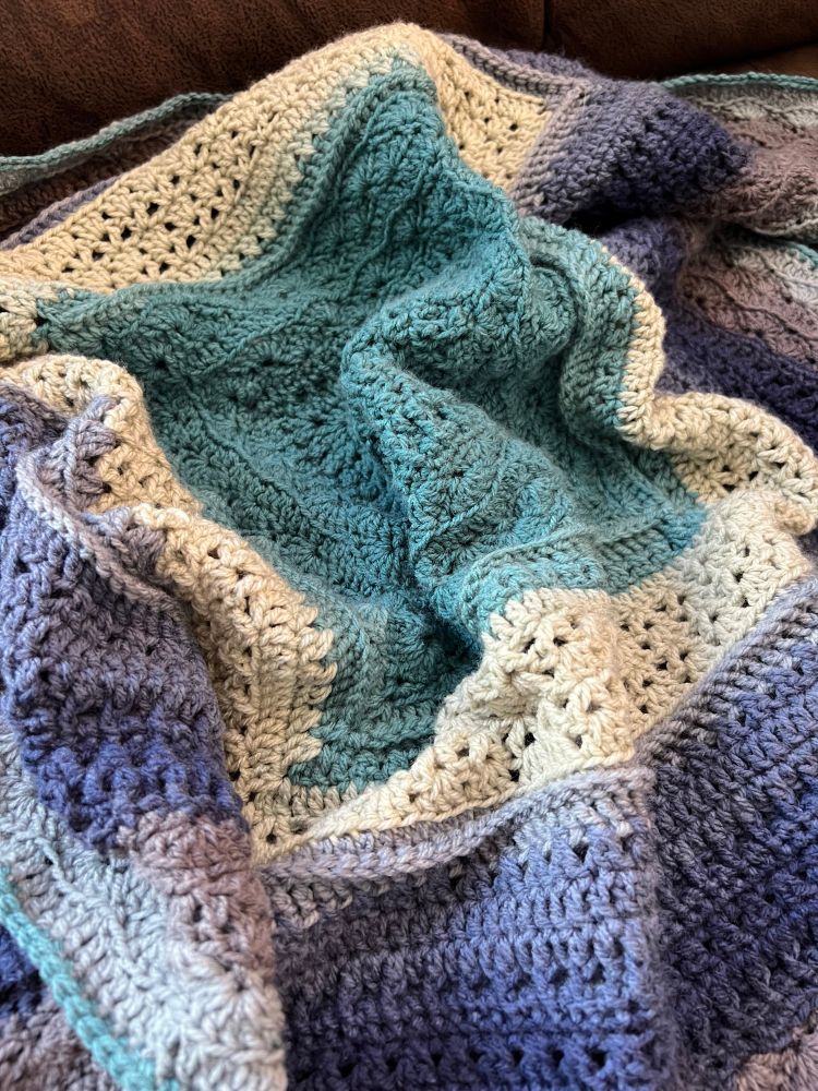 A photo of a baby blanket in shades of blue, green, and grey 