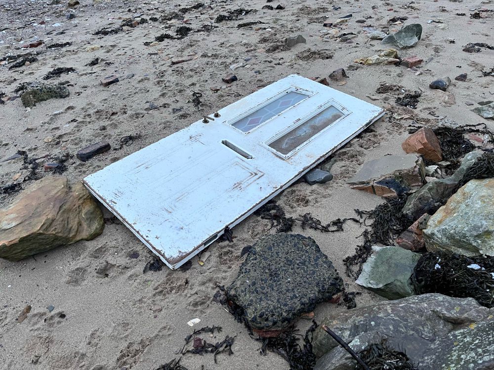 White external door, with two narrow panes of glass & letterbox, washed up and lying flat on sand of the Fife foreshore.