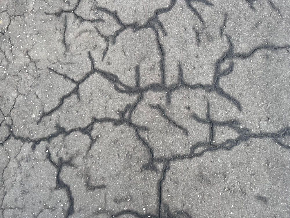 Cracks in an asphalt pavement with water ingress creating a network of dark interlocking lines