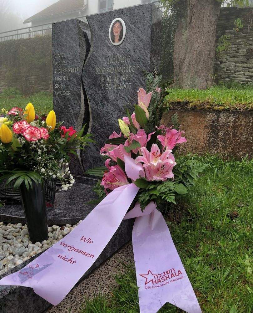 Das Grab von Michéle Kiesewetter. Davor mehrere Blumen, ein Gesteck de Haskala mit der Aufschrift „Wir vergessen nicht“. Auf dem Grabstein ist ein Foto von ihr, dazu ihr Geburts- und Sterbedatum. Dazu steht „UND ALLES
GETRENNTE
FINDET SICH
WIEDER“ 