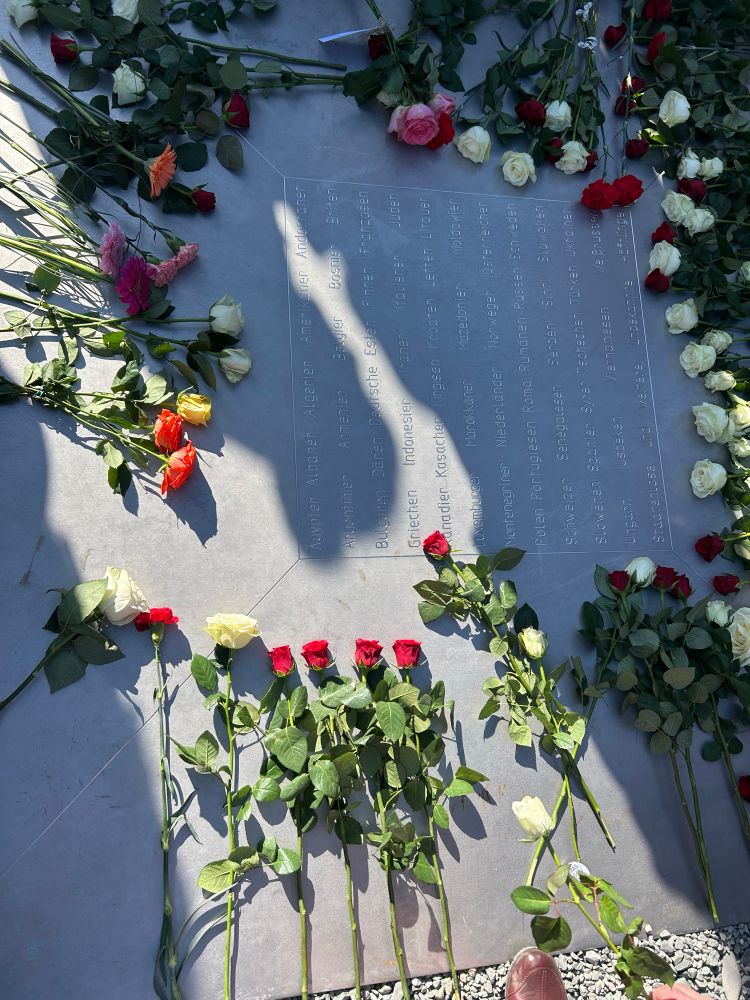 Erinnerungsort mit eingravierten Herkunftsländern der in Buchenwald ermordeten auf dem Appellplatz in Buchenwald. Rings um die eingravierungen liegen weiße und rote Rosen.  
