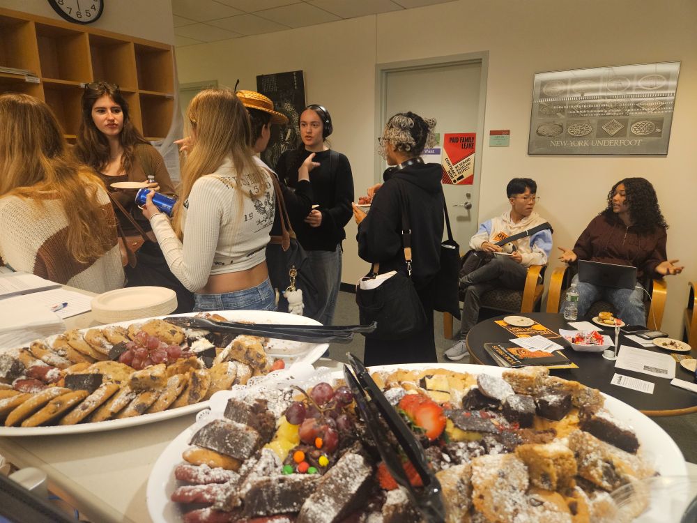 Students and faculty chat in small groups in the history department office with platters of baked goods in the foreground.
