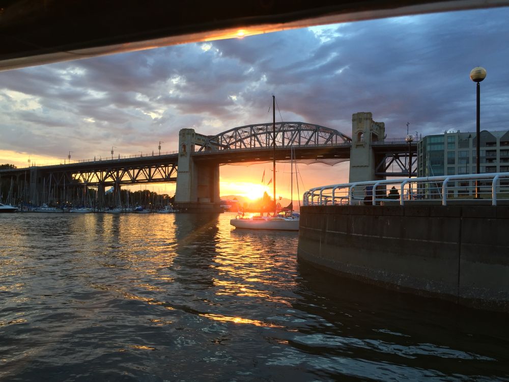 Photograph shows bridge over a river with setting sun just above the horizon