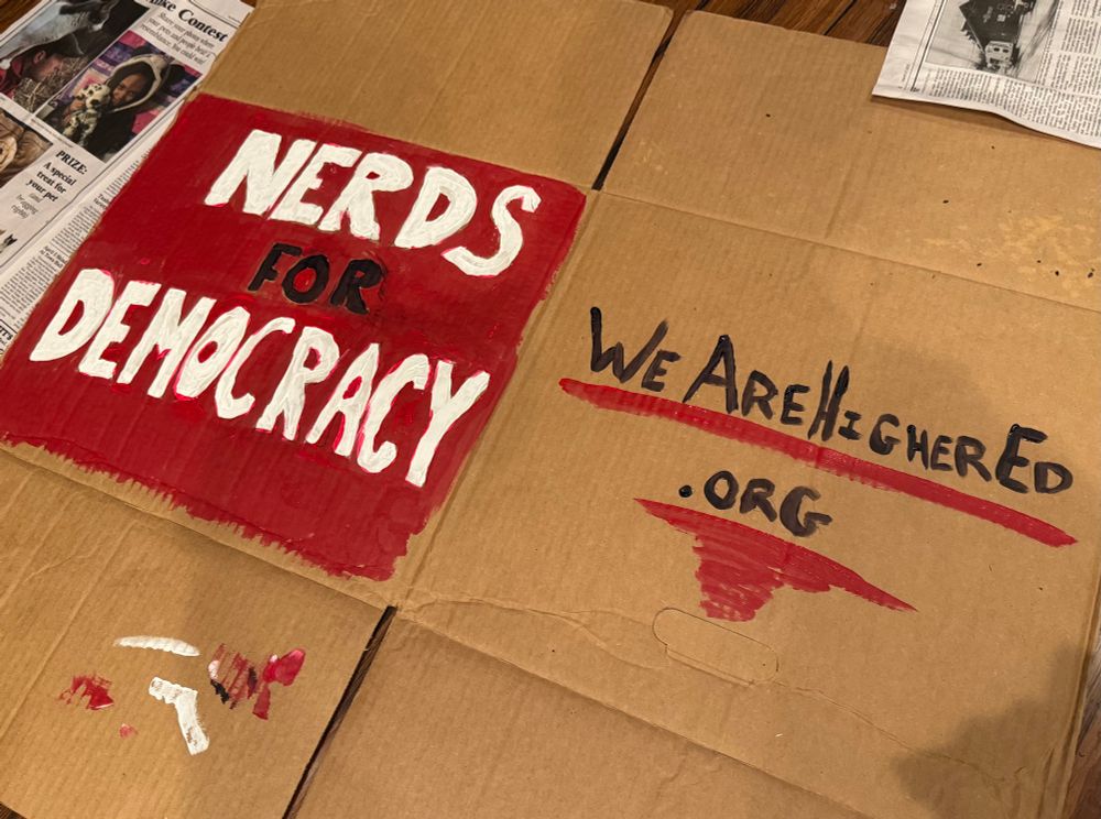Cardboard painted with “nerds for democracy” on one side and “wearehighered.org” on the other in black, red, and white