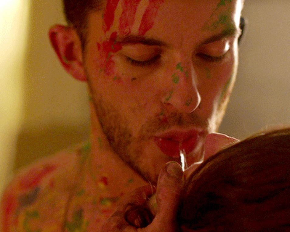 Close up of Sam from Crashing spilling vodka into Lulu’s mouth. He is very focused and covered in paint. 