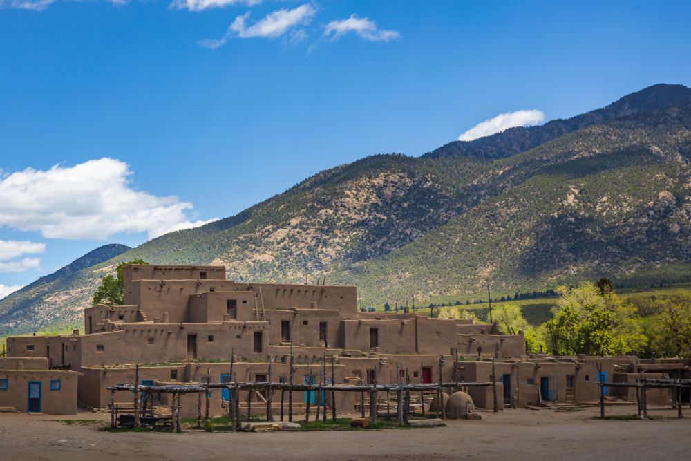 Photo of Taos Pueblo with mountains rising behind the building