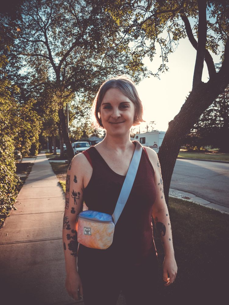 Photo of Jen walking on a tree lined street with sunbeams wearing tank top, yoga pants and fanny pack. 