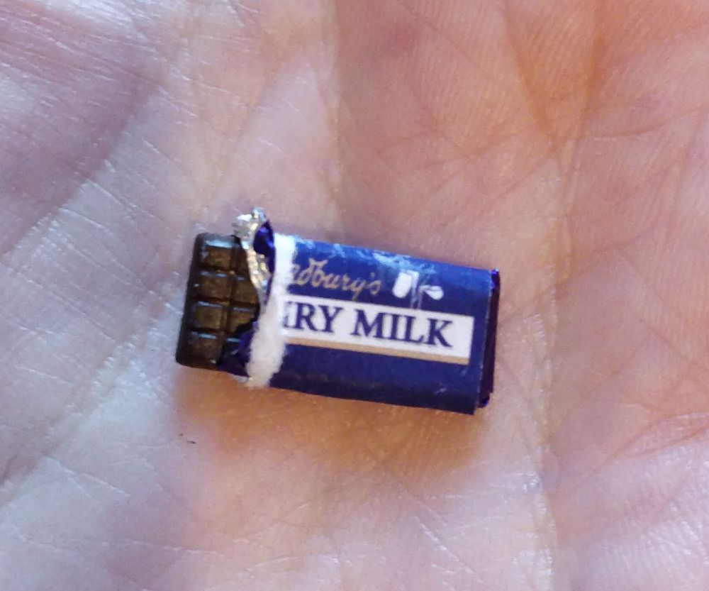 Chocolate con leche de Cadbury's en miniatura sobre la palma de la mano. Está un poco a abierto, con el envoltorio rasgado y se ve el papel metálico que lo envuelve.