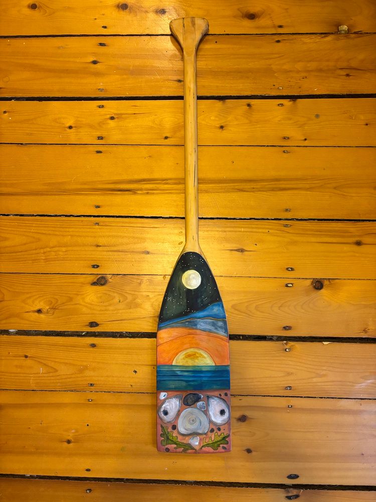 A child’s canoe paddle painted with a moon, sunrise over water and some seashells/seaweed. Very folk arty. 