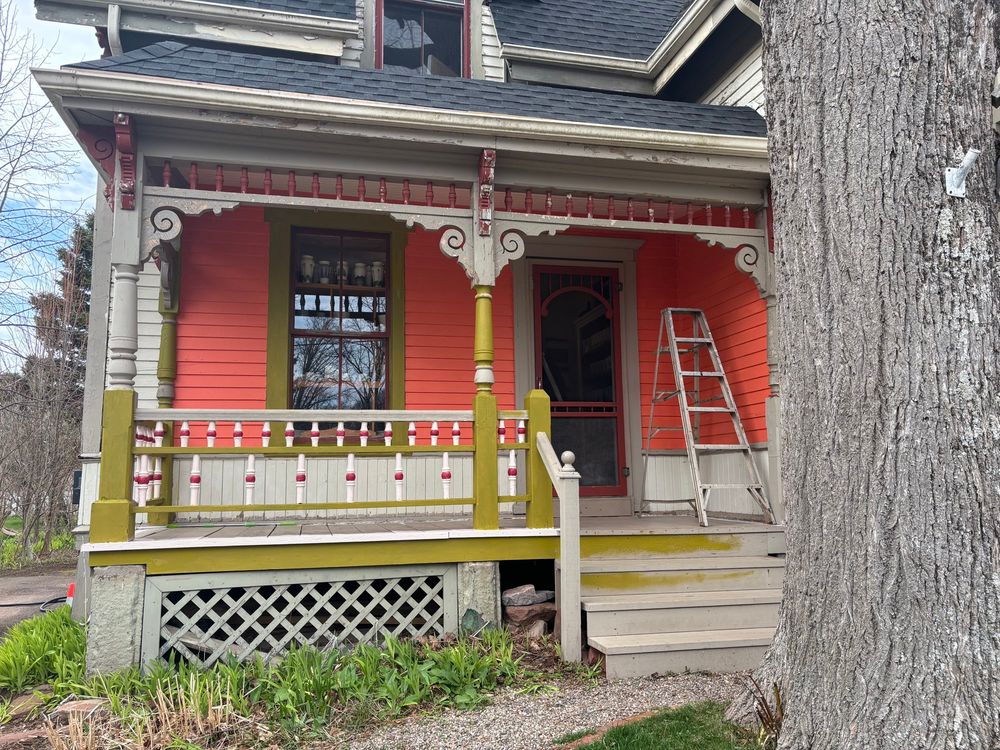 The outdoor porch of a beige Victorian house that is being painted orange, green, peach and raspberry. 