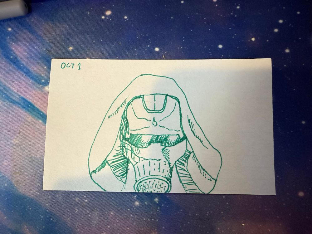 A hand-drawn illustration of a hooded figure wearing goggles and a mask, sketched in green ink on a piece of white paper. The top left corner features the text "OCT 1." The desk mat it is lying on has a galaxy-themed pattern.