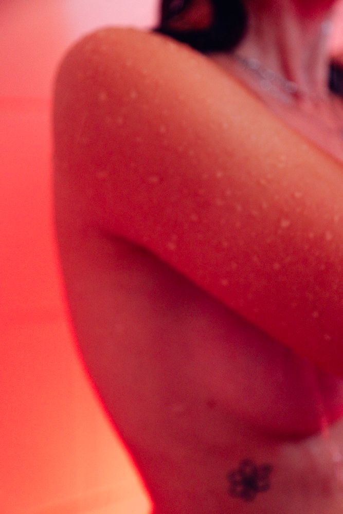 Détails flou de corps féminin sous la douche. La lumière est chaude et intense, rouge et acidulée.