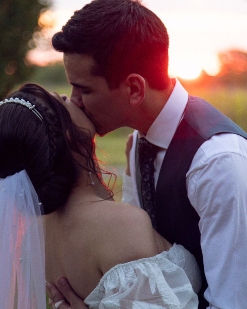 Un couple s’embrasse tendrement au coucher du soleil, le jour de leur mariage. L’ambiance est douce et romantique.