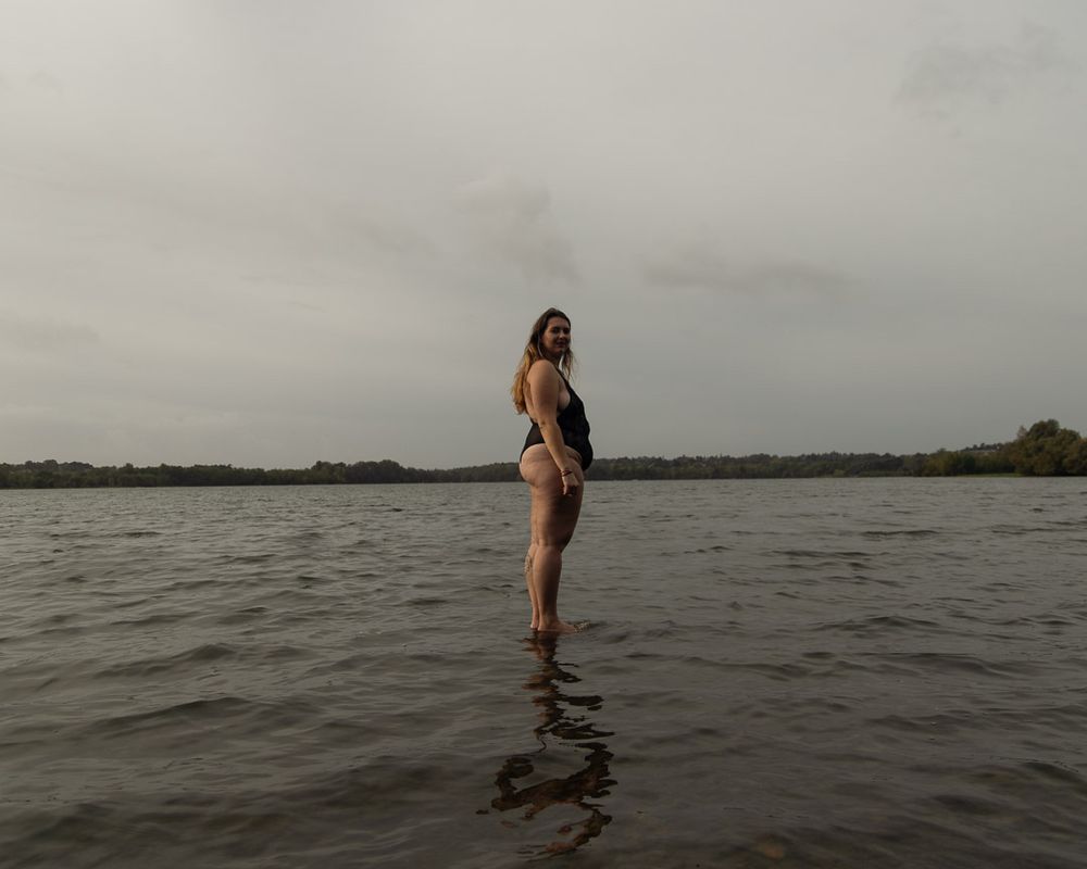 Silhouette féminine vue de côté et droite comme un i, en body noir, se tournant vers le spectateur. La lumière grise et orageuse contraste avec la légèreté du moment. 