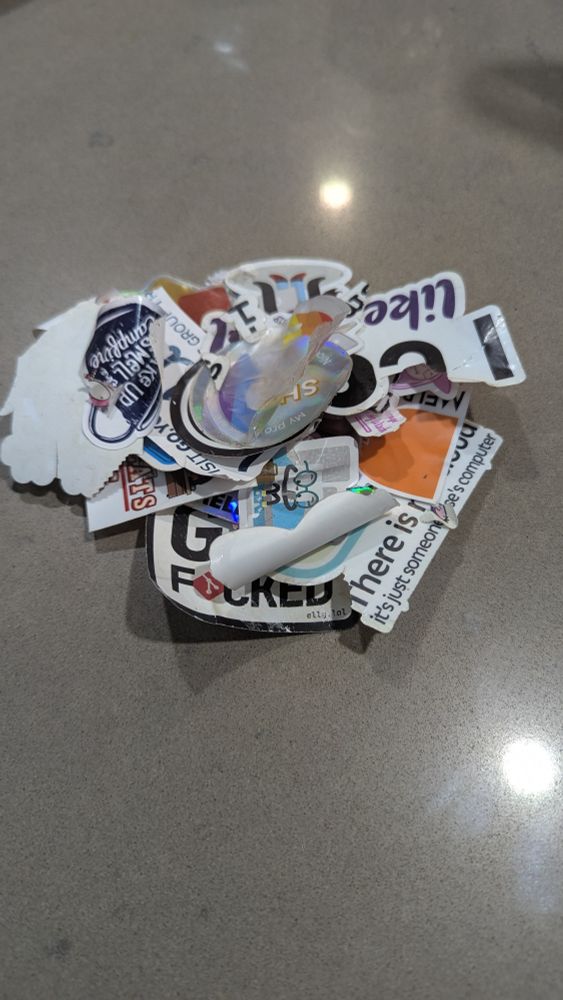 The photo shows a pile of torn and curled up stickers that have been removed recently from a surface. Mostly tech and programmer related stickers.