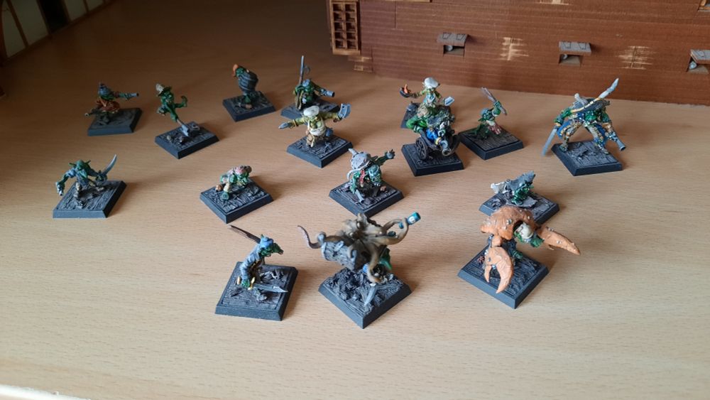 Some Freebooters Fate Goblin Miniatures standing on a wooden shelf top. Behind them a small part of an MDF Ship set.