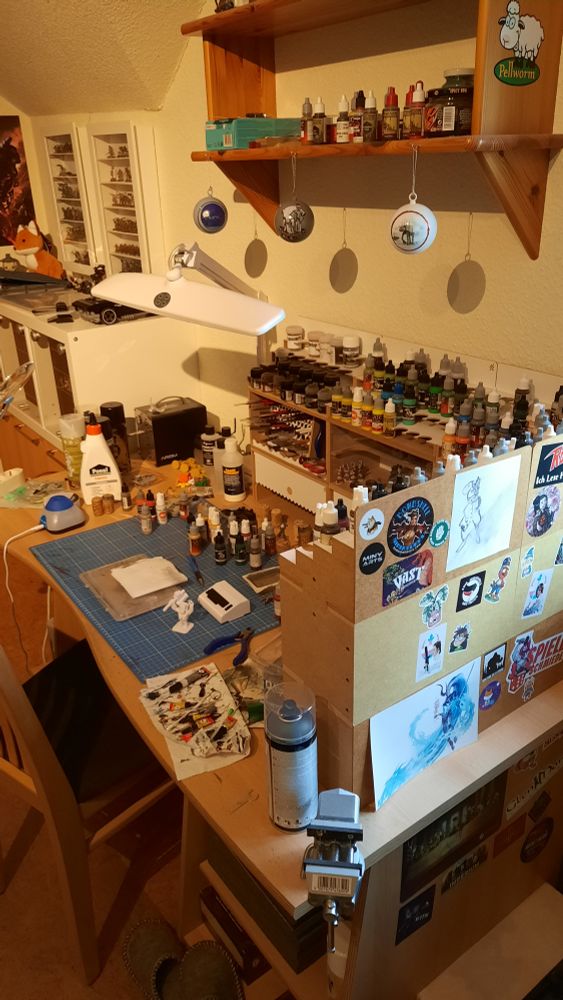 The picture shows my hobby desk with some Hobbyzone Painting station components, the back side filled with hobby stickers. Above the desk is a shelf with Star Wars christmas tree balls attached to it. In the background some displays for miniatures. 