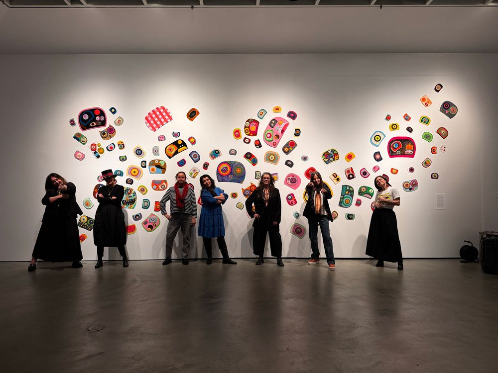 7 artists posing in front of ovoid artwork on wall by Charlene Lickers