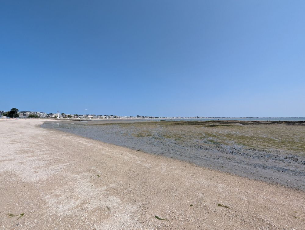 A vast white sand and she'll beach, currently at very low tide. The seaside condos and hotels of La Baul are visible in the distance, as is the Atlantic ocean.