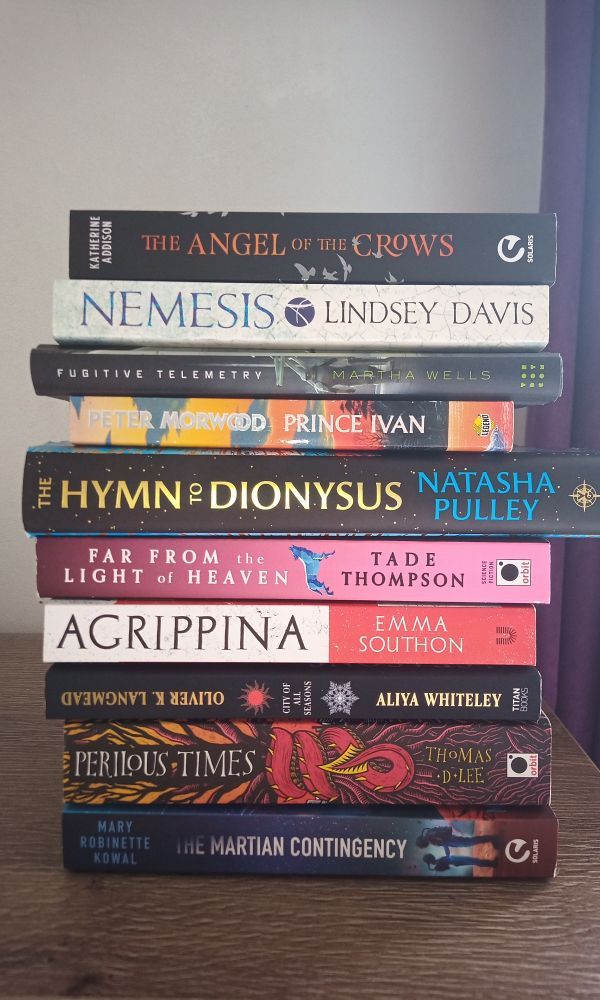 A stack of books, from top to bottom:
The Angel of the Crows by Katherine Addison
Nemesis by Lindsey Davis (actually standing in for the whole Didius Falco series)
Fugitive Telemetry by Martha Wells
Prince Ivan by Peter Morwood (#GNUPeterMorwood)
The Hymn to Dionysus by Natasha Pulley
Far From the Light of Heaven by Tade Thompson
Agrippina by Emma Southon
City of All Seasons by Oliver Langmead and Aliya Whiteley
Perilous Times by Thomas D Lee
The Martian Contingency by Mary Robinette Kowal 