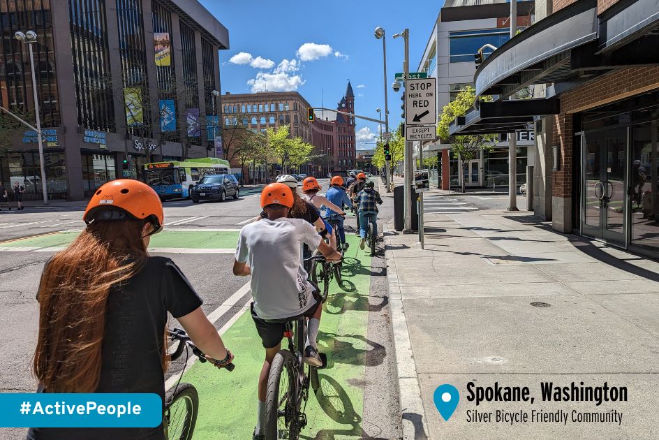Young people in orange helmets ride in a green bike lane in Spokane, Washington, a Silver-level Bicycle Friendly Community. 
