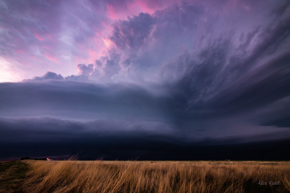 Photo of a supercell thunderstorm over a prairie field at sunset with purple/pink hues near Garden City, Kansas on May 24, 2021.